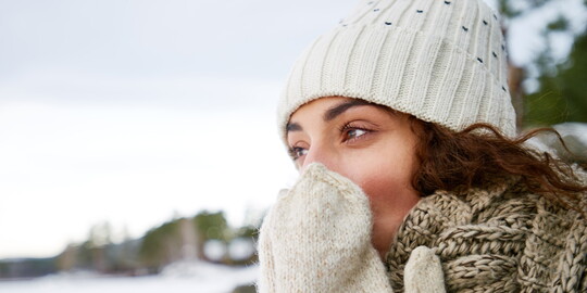 Frau im Winter mit Mütze und Handschuhen, hält sich ihre Hand an die anscheinend kalte Nase