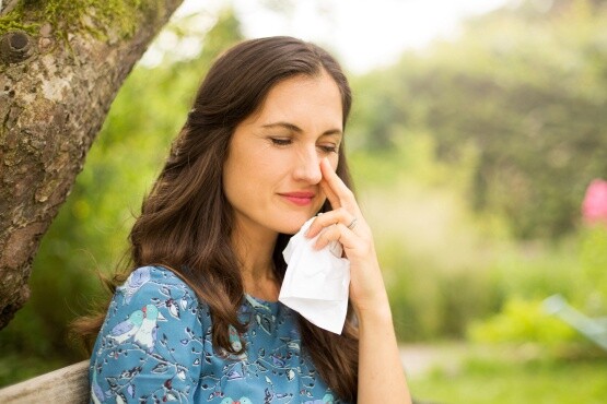 Frau mit Heuschnupfen / Pollenallergie fässt sich an die Nase